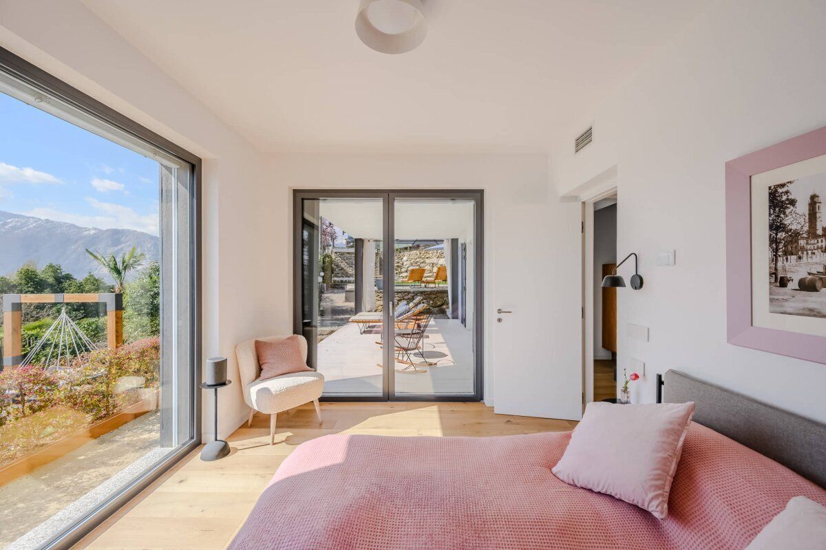 Een slaapkamer met een groot bed, een schuifdeur naar een terras buiten en uitzicht op bergen.