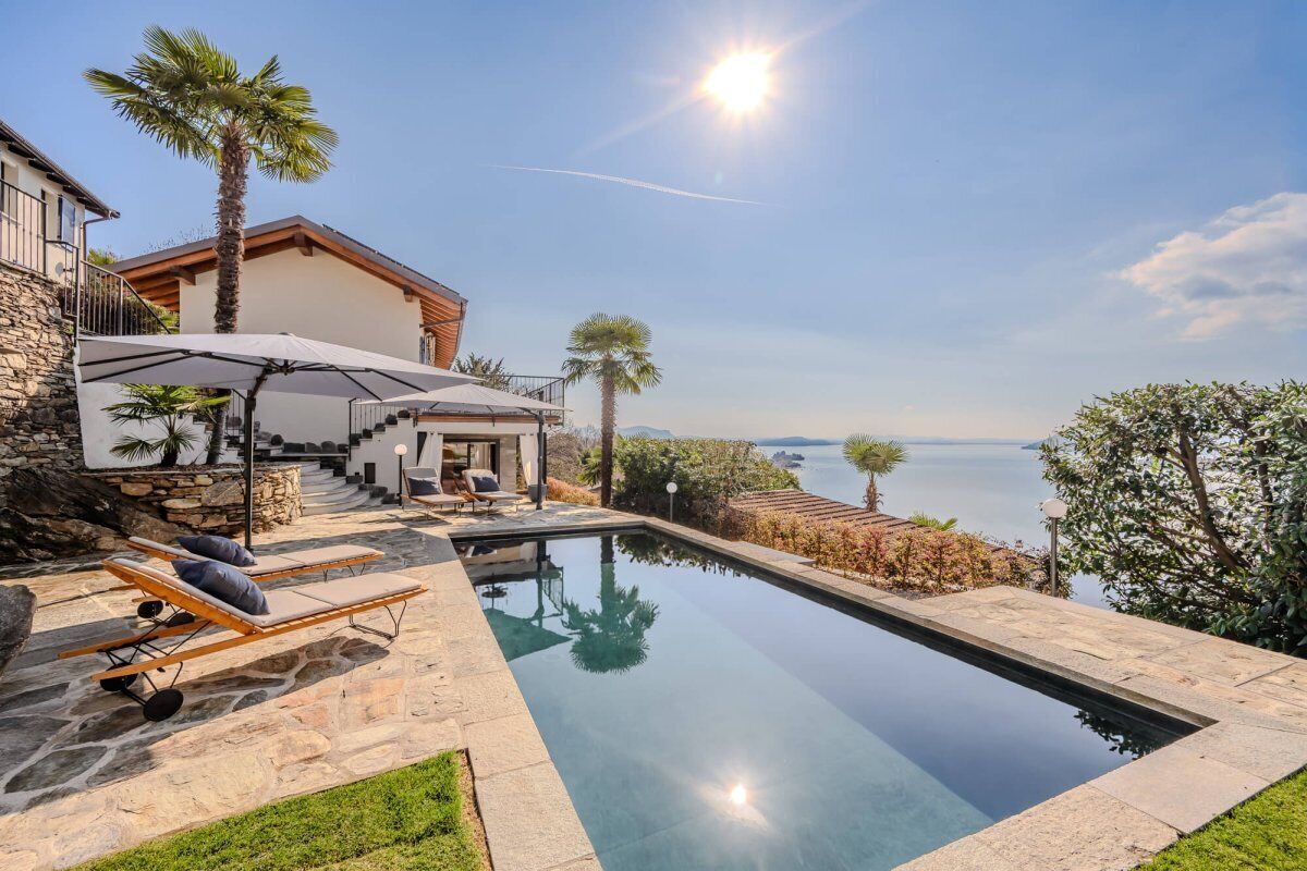 A poolside area with lounge chairs, a stone wall, and a view of the sea.