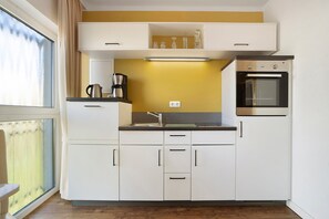 Une cuisine compacte avec des meubles blancs, un four encastré et une fenêtre avec des rideaux.