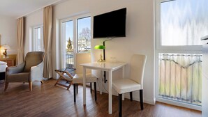 Una habitación con cama, escritorio, silla, televisor y ventanas amplias.