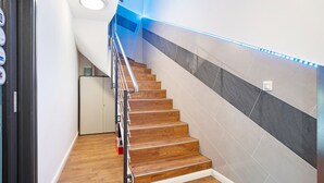 Una escalera de madera con barandilla de metal que lleva a un rellano con una puerta blanca y un estante pequeño.