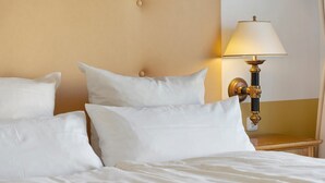 Una cama con ropa de cama y almohadas blancas, una mesita de noche con una lámpara y una pared con textura.