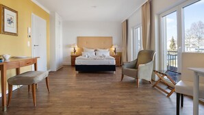 Una habitación de hotel con cama, escritorio, silla, una mesita y ventanas amplias.