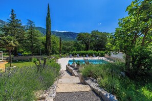 A pool area with a stone pathway leading to lounge chairs, surrounded by greenery and mountains in the background. - Vacation apartment for up to 6 people with pool and idyllic location (Tribalj)
