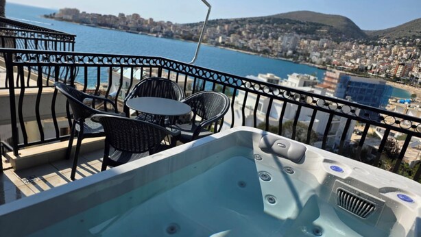 Un balcone con idromassaggio, sedie e un tavolo con vista sulla città e sul mare.