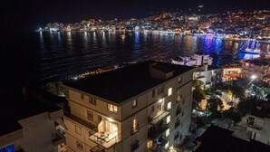Una vista notturna di una città costiera con edifici illuminati, un lungomare e una ruota panoramica ben visibile.