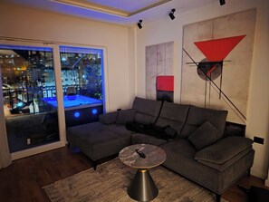 Een moderne woonkamer met een hoekbank, een glazen deur naar een balkon en een eigentijds kunstwerk aan de muur.