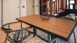Zona pranzo moderna con tavolo in legno, sedie nere e una scala con ringhiere in legno.