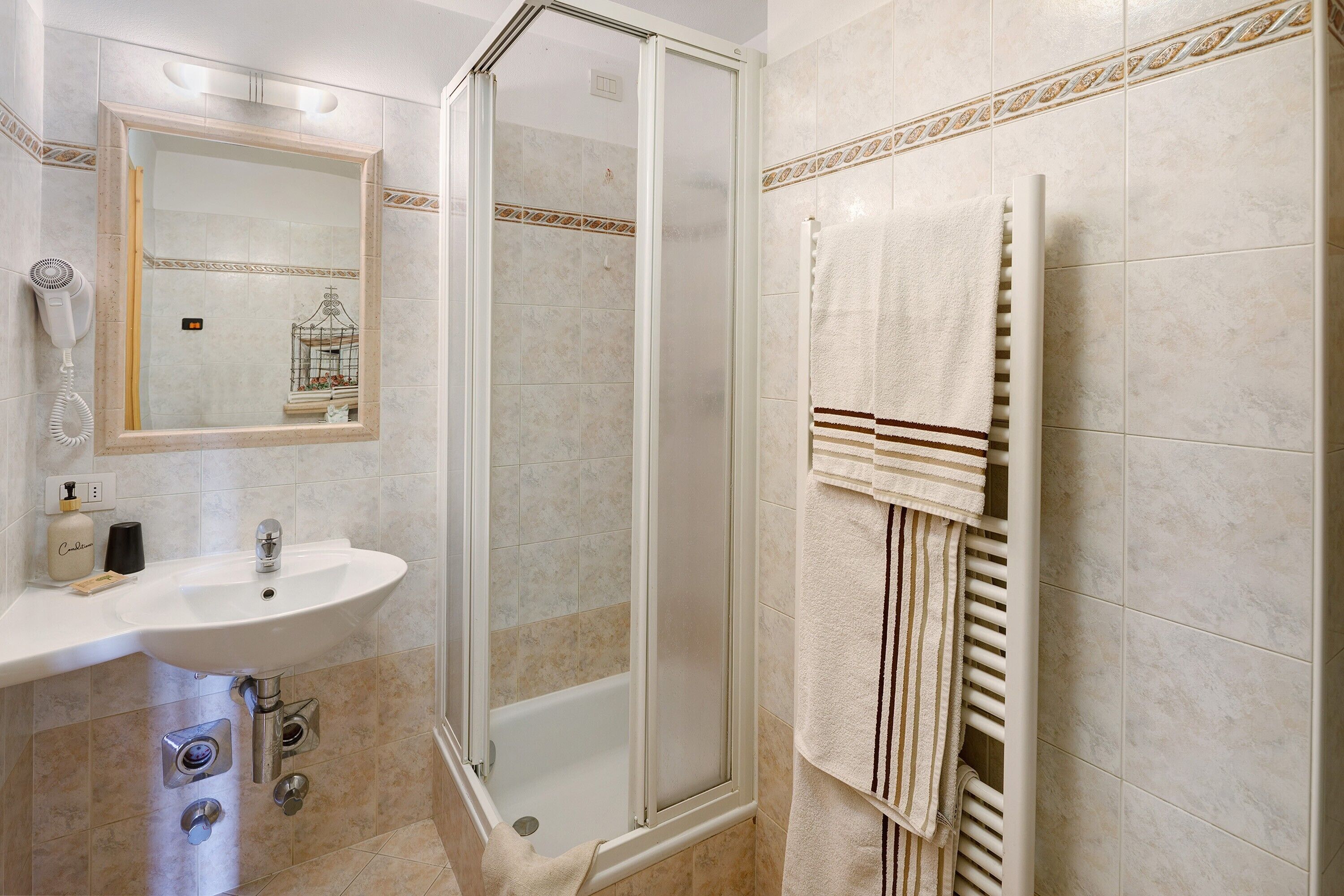 A bathroom with a glass-enclosed shower, a sink, a mirror, and a towel rack.