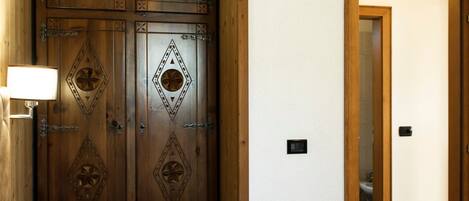 A bedroom with a wooden wardrobe, a bed with patterned bedding, and a nightstand with a lamp.