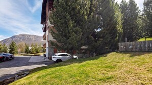 A building with a sloped roof, parked cars, and a grassy area with trees. - Apartment 1 Shared Garden and Wi-Fi (Teola)