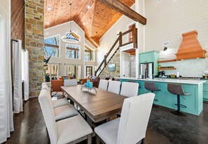 A spacious dining area with a wooden table and chairs, a kitchen with teal cabinets, and a stone accent wall. - Waterfront Group Retreat with Pickleball (Broken Bow)