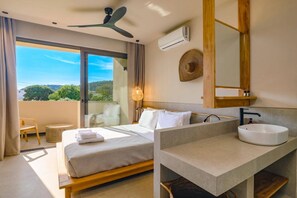 Habitació d'hotel moderna amb un llit, un bany amb un rentapins i una finestra gran que ofereix vistes a la vegetació.