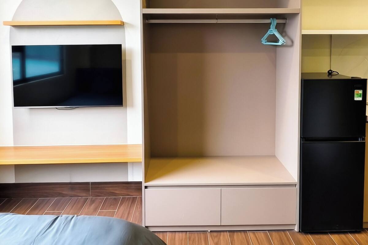 Une chambre à coucher comprenant un lit, un téléviseur fixé au mur, une armoire et un réfrigérateur.