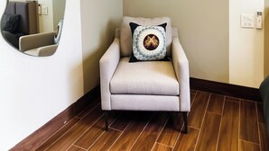 A room with a wooden floor, a beige armchair with a patterned pillow, a wall-mounted air conditioner, and a large mirror. - Klara House Phuc Dong (Hanoi)