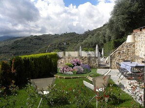 Ein angelegter Garten mit einer Steinmauer, Sitzgelegenheiten im Freien und Blick auf eine hügelige Landschaft.