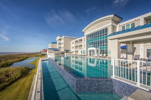 Hotel com piscina, espreguiçadeiras e vista para o mar.