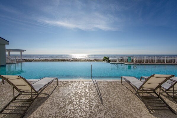 Piscina com espreguiçadeiras, vista para o oceano e céu claro.