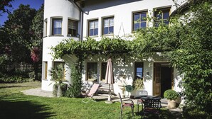 A two-story house with a covered porch, outdoor seating, and a garden.