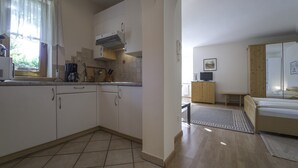 A compact kitchen with a coffee maker, a stove, and a window with curtains.
