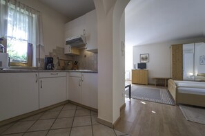 A compact kitchen with a coffee maker, a stove, and a window with curtains. - 741A Gwürzerhof Apartment (Termeno sulla strada del vino)