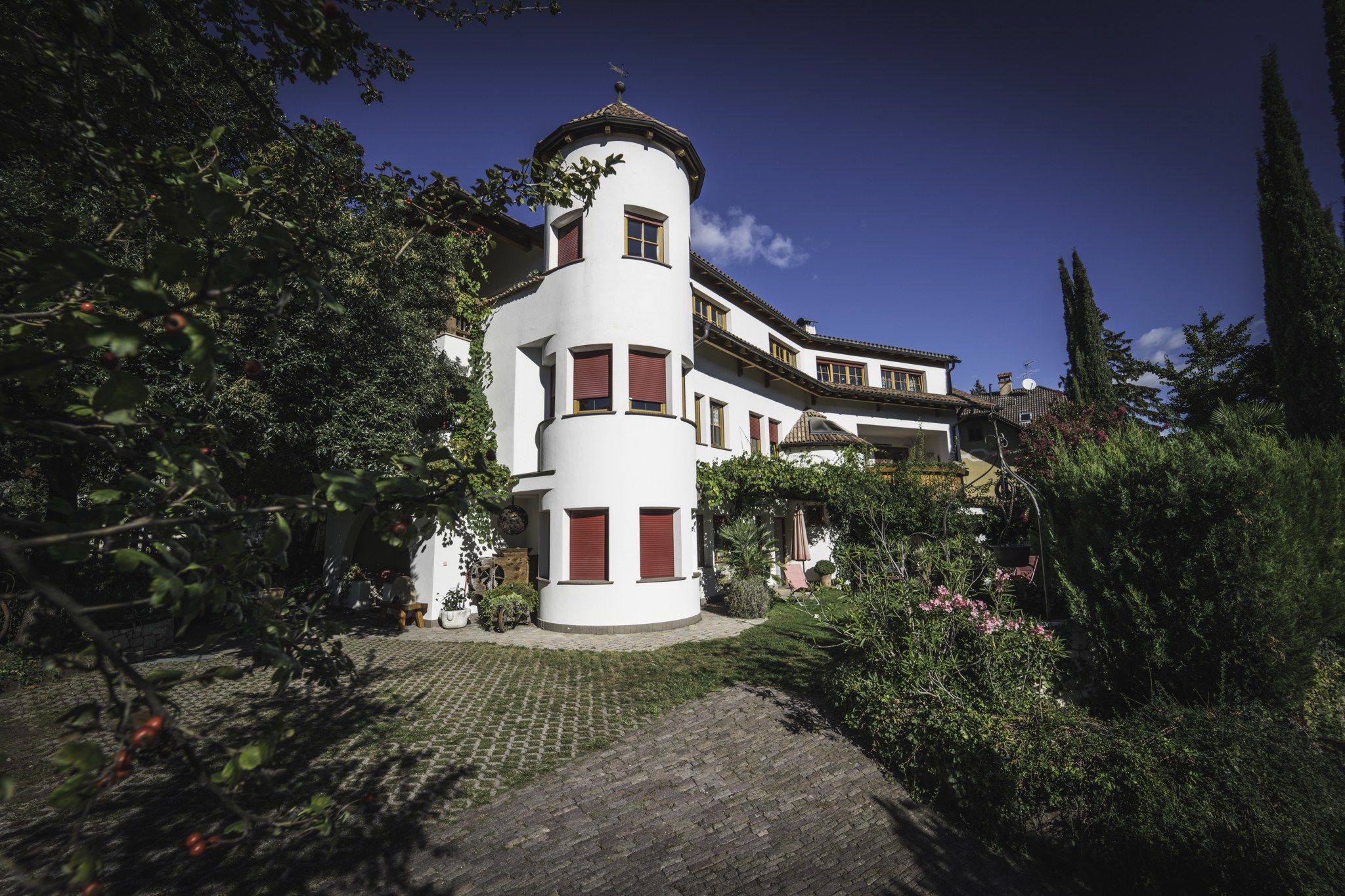 Un edifici blanc amb una torre circular, envoltat de vegetació abundant i un camí empedrat.