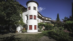A multi-story building with a cylindrical tower, surrounded by greenery and a cobblestone pathway.