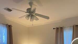Un dormitorio con cama, ventilador de techo, mesita de noche y espejo.