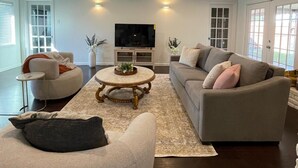Un salón amplio con un sofá grande de color gris, una mesa redonda de centro y un televisor de pantalla plana.