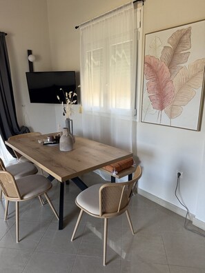 Ein Essbereich mit einem Holztisch, vier Stühlen, einer Vase mit Blumen, einem Flachbildfernseher und einem großen Wandbild mit Blattmotiven.