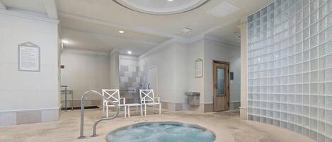 Zona de spa con jacuzzi, sillas blancas y pared con azulejos.