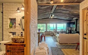 Ein Zimmer mit weißer Ziegelwand, einer Holztür, einem weißen Sofa, einem Esstisch mit Stühlen und Blick durch große Fenster.