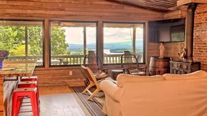 Uma cabana aconchegante com interior de madeira, uma janela grande com vista para uma paisagem deslumbrante, uma lareira e uma área de estar confortável.