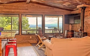 Ein gemütliches Blockhaus mit Holzvertäfelung, einem großen Fenster mit Blick auf eine reizvolle Landschaft, einem Kamin und einer komfortablen Sitzecke.