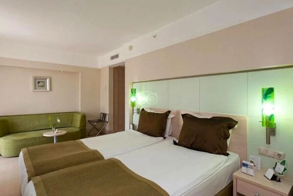 A hotel room with a bed, a green sofa, a small table, and a nightstand with a lamp. - Ambassador Plaza Hotel (Kemer)