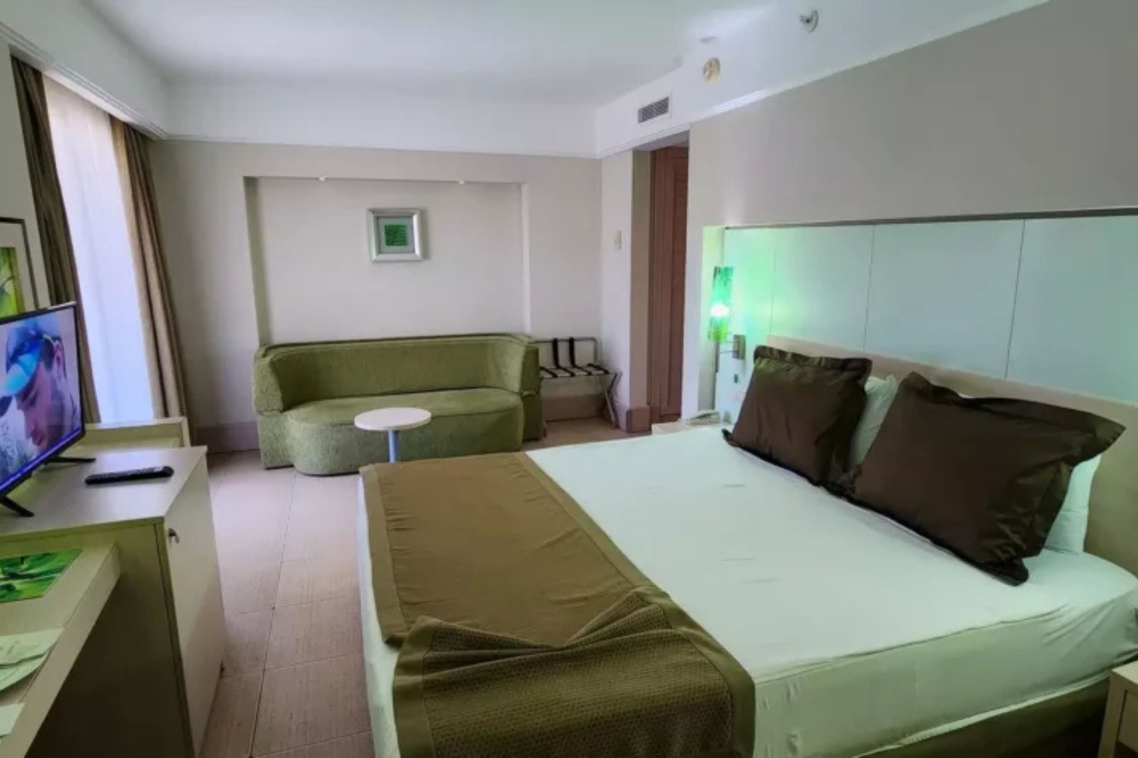 A hotel room with a bed, a television, a small table, and a sofa.