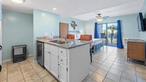 Una cocina con una isla central, armarios blancos, un lavabo y una zona de comedor con mesa y sillas.