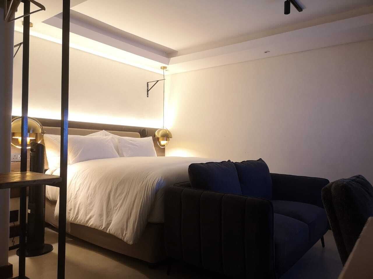 A hotel room with a bed, a sofa, a table, and a lamp.