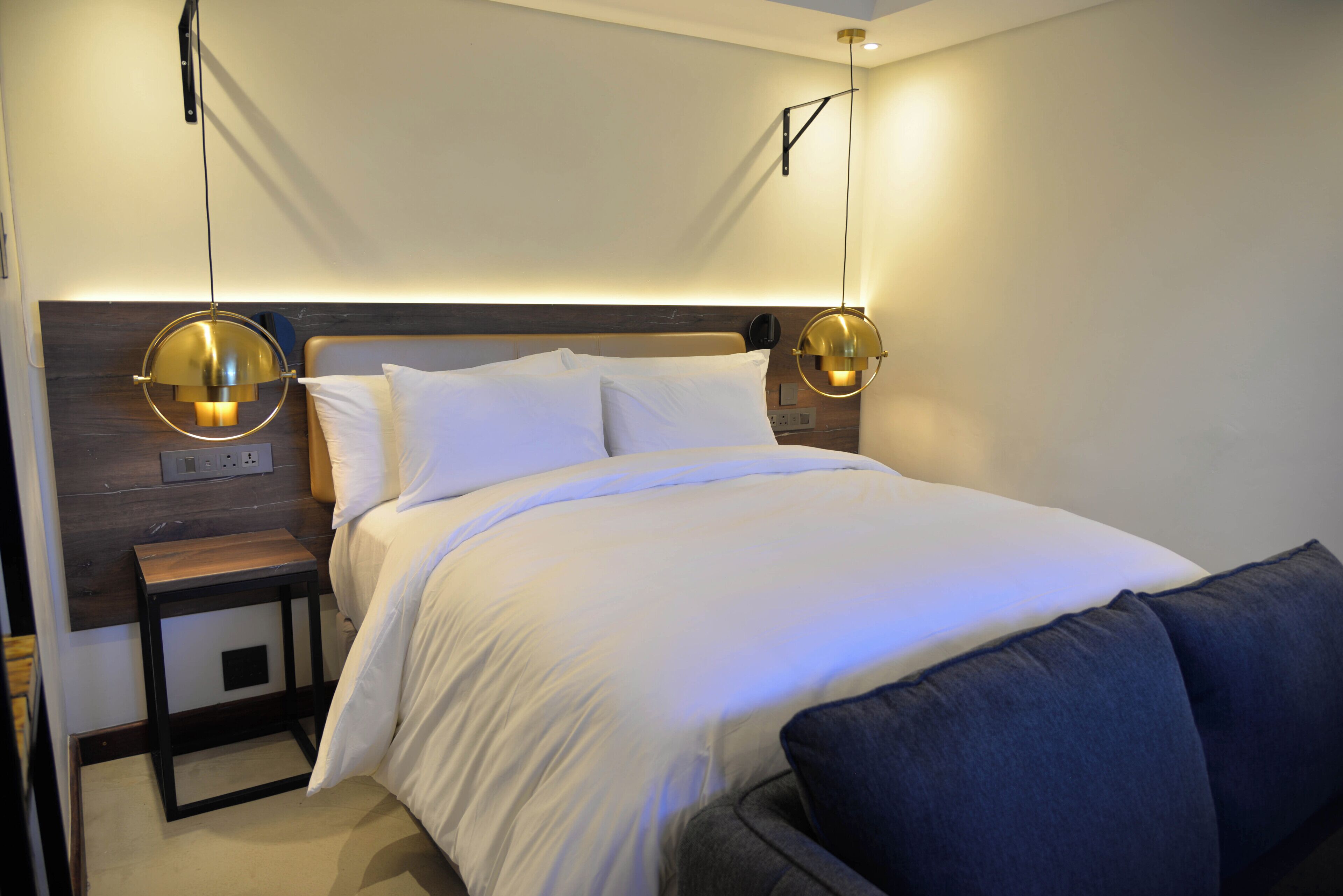 Una habitació d'hotel moderna amb un llit ben fet, taules de nit i il·luminació penjada a la paret.