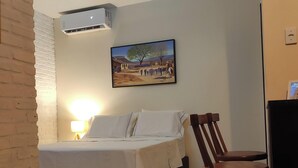 Quarto com cama, cadeira, aparelho de ar condicionado, um quadro na parede e luminária.