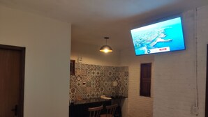 Quarto com televisão presa na parede, painel de fundo trabalhado e luminária pendente.
