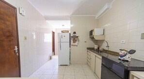 A kitchen with white tiled walls, a refrigerator, a microwave, a sink, and a dishwasher. - Apto em Praia Grande Frente a Praia da Guilhermina (Praia Grande)