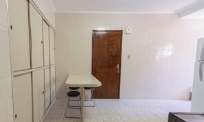 A small kitchen with a wooden door, a white tiled wall, and a table with stools. - Apto em Praia Grande Frente a Praia da Guilhermina (Praia Grande)