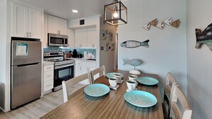 A modern kitchen with white cabinets, stainless steel appliances, and a wooden dining table with teal plates. - Victorian 9124 - Good Times & Tan Lines (Galveston)