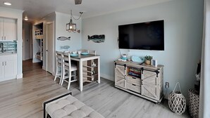 A modern living room with a dining area, wooden flooring, a flat-screen TV, and a decorative fish wall art. - Victorian 9124 - Good Times & Tan Lines (Galveston)