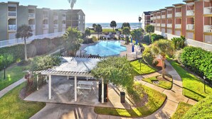 A pool area with a pergola, a view of the ocean, and a parking lot. - Victorian 9124 - Good Times & Tan Lines (Galveston)