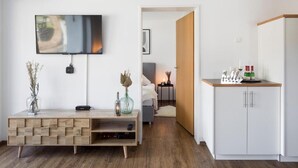 Quarto moderno com televisão de tela plana, mesa de console de madeira, armário branco e cama com mesa de cabeceira.
