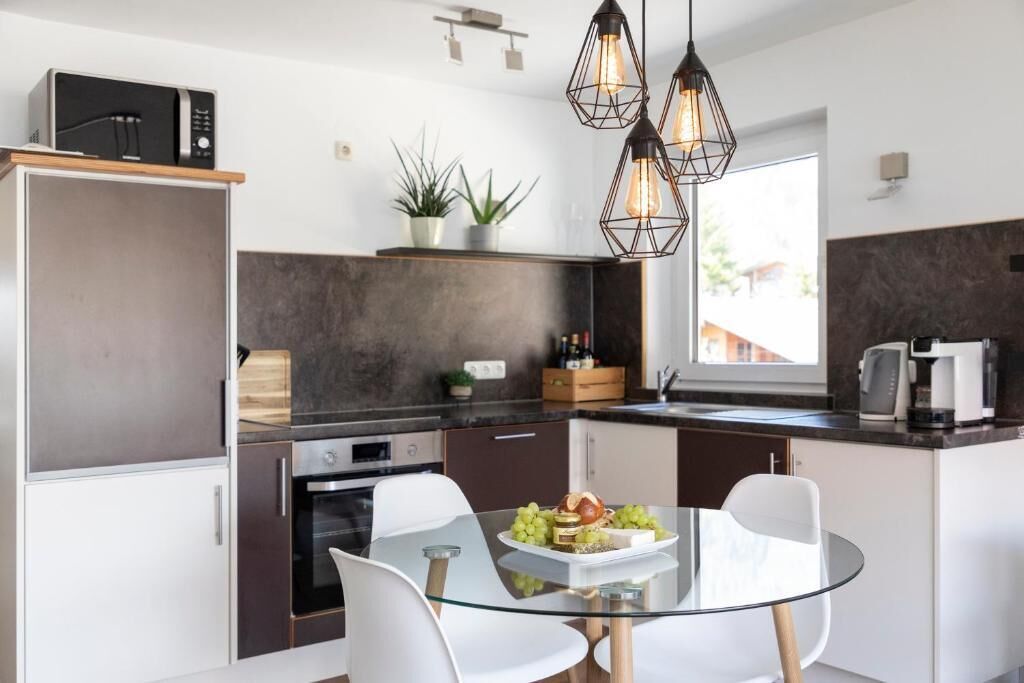 A modern kitchen with a glass dining table, white chairs, and pendant lighting.
