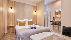 A modern bedroom with a bed, bedside tables, a bench, a bathroom with a sink and mirror, and a fireplace. - Beautiful apartment in the heart of Paris 10 people (Paris)