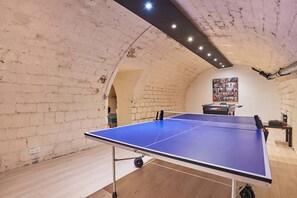 Ein Tischtennistisch in einem Raum mit unverputzten Ziegelwänden und einer Decke mit sichtbaren Holzbalken.